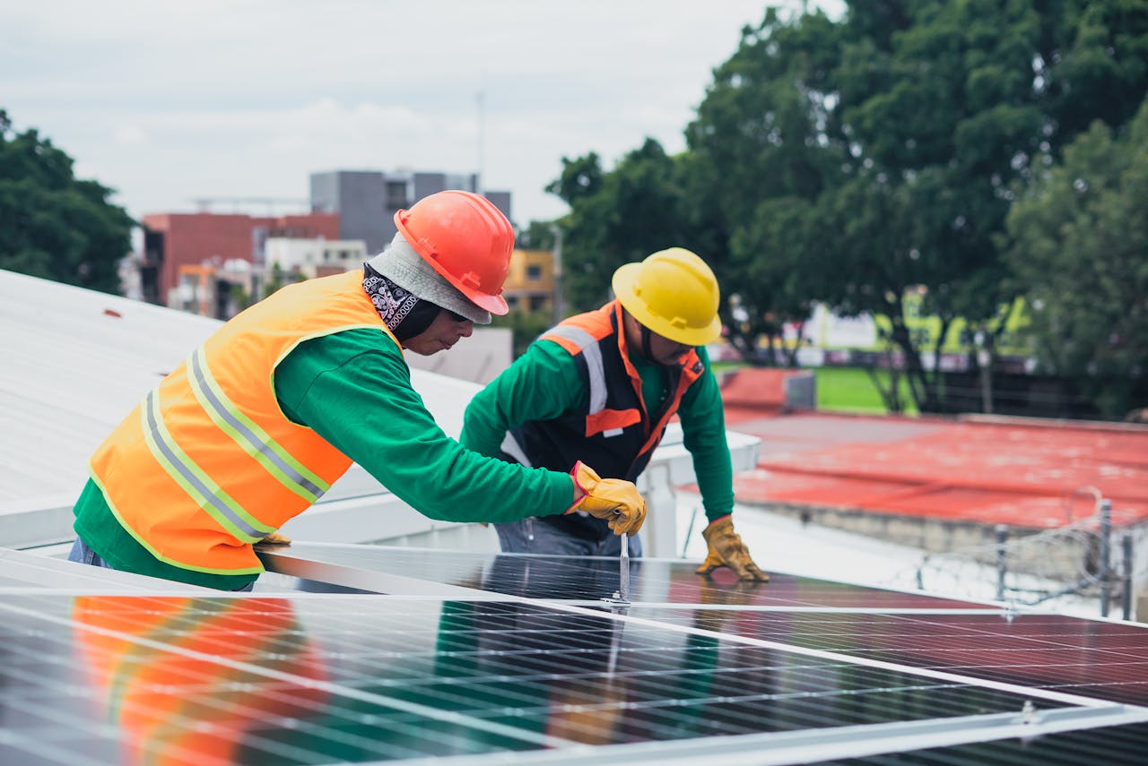 Servicios Two workers installing rooftop solar panels safely equipped with PPE and tools.